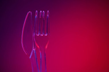 Kırmızı arka planda plastik şeffaf çatal ve bıçak.