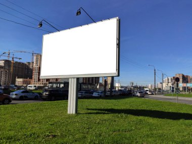 Şehirdeki büyük reklam panoları yeşil bir çimenlikte ve mavi gökyüzüne karşı.