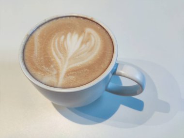 Bir fincan kapuçino, beyaz arka planda kalp şeklinde bir kahve.