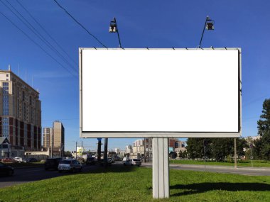 Şehirdeki büyük reklam panoları yeşil bir çimenlikte ve mavi gökyüzüne karşı.