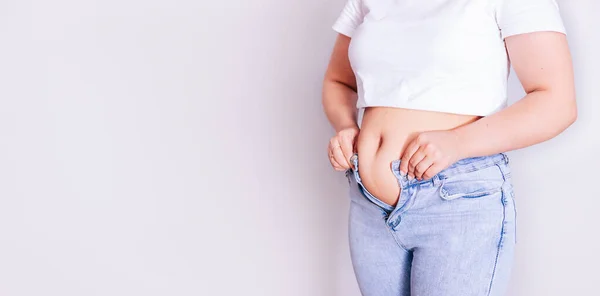 A woman dresses in jeans after giving birth. The concept of the diet-close-up of womens hands can not button their pants because of the increase in fat on the thighs after childbirth — Stock Photo, Image