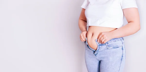 Una mujer se viste de vaqueros después de dar a luz. El concepto de la dieta-primer plano de las manos de las mujeres no pueden abotonarse los pantalones debido al aumento de la grasa en los muslos después del parto — Foto de Stock