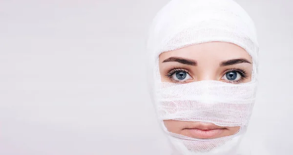 Ameliyat sonrası yüzü bandajlı bir kızın beyaz bir arka planı var. Test için uygun bir yer.