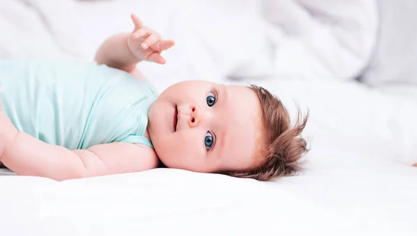 Een pasgeboren baby ligt op een sneeuwwit bed. Een prachtig kind van Europees uiterlijk. Gezond slapen, wakker worden, en wakker worden in de ochtend. — Stockfoto