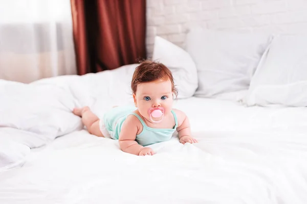 一个手里拿着奶嘴的新生婴儿躺在雪白的床上 — 图库照片