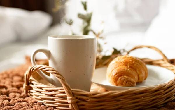 Breakfast tray on the bed in the hotel room. breakfast in a snow-white bed, coffee with a croissant on a wicker tray. Morning.