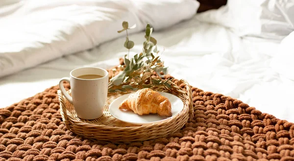 Breakfast tray on the bed in the hotel room. breakfast in a snow-white bed, coffee with a croissant on a wicker tray. Morning.