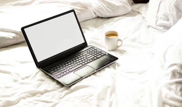 an open laptop with a cup of tea lying on a white bed. breakfast in bed with a laptop with a cup of coffee .