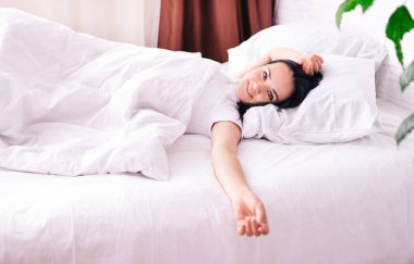 Odada kar beyazı bir yatakta uzanmış gülümseyen güzel bir kızın görüntüsü..