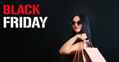 Elinde alışveriş çantası olan ve siyah gözlüklü güzel bir müşteri Kara Cuma tatilinde siyah bir arka planda izole edilmiş. Metin için boşluk