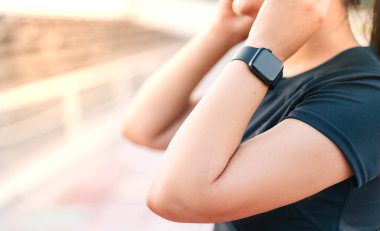 Sabahleyin stadyumda dikilen esmer bir koşucunun yan görüntüsü. Spor ekipmanları içinde bir kadın, yolda dikilip kulaklıkla müzik dinliyor. yakın plan