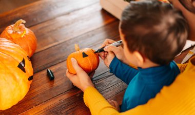 Mutlu bir aile Cadılar Bayramı için hazırlanıyor. güzel genç bir anne ve oğlu evde siyah bir kalemle bir balkabağı yüzü çiziyor.