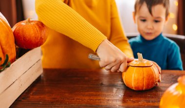 Mutlu bir aile Cadılar Bayramı için hazırlanıyor. Güzel genç bir anne ve oğlu evde balkabağı oyuyor.