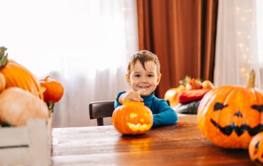 Güzel küçük bir çocuk Cadılar Bayramı için dekore edilmiş bir arka plana balkabağı oyup gülümsüyor..