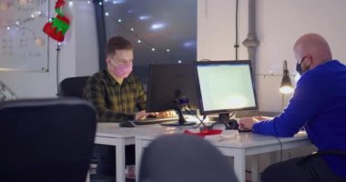 Maskeli adamlar açık uzay ofisindeki bilgisayarlarda çalışıyor.