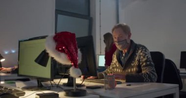 Yüz maskeli bir adam geceleri bilgisayar başında çalışıyor.