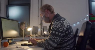 Yüz maskeli bir adam geceleri bilgisayar başında çalışıyor.