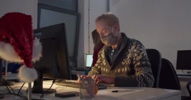 Yüz maskeli bir adam geceleri bilgisayar başında çalışıyor.