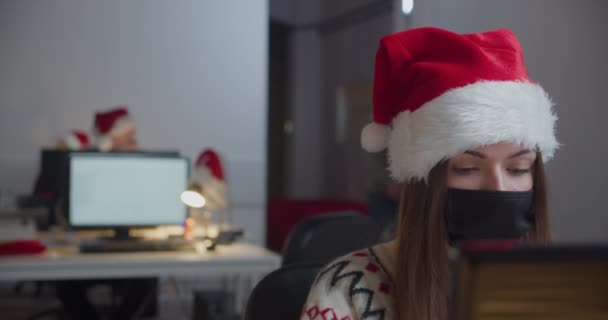 戴着面具和圣诞老人帽的女人晚上在办公室工作 — 图库视频影像