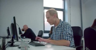 Ofiste çalışan kızıl işadamı ve arkasında iş arkadaşları 