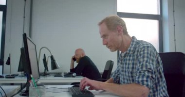 Ofiste çalışan kızıl işadamı ve arkasında iş arkadaşları 