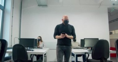 Kel işadamı maske takıyor ve iş sırasında işçilerini izliyor.