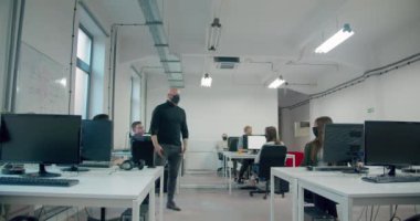 Kel işadamı maske takıyor ve iş sırasında işçilerini izliyor.