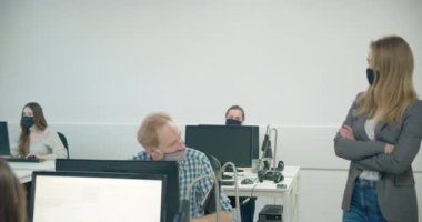 Kadın patron maske takıyor ve çalışanlarını iş başında izliyor. 