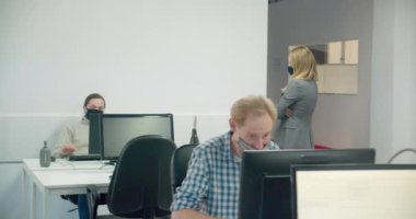 Kadın patron maske takıyor ve çalışanlarını iş başında izliyor. 