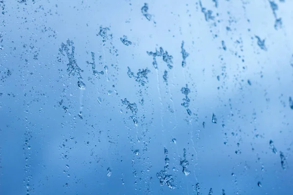 在暴风雨的蓝天的衬托下，玻璃杯上的雨与雪的流淌在一起 — 图库照片