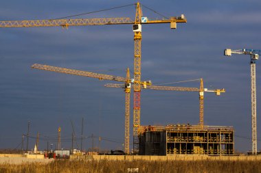 Koyu mavi gökyüzüne karşı tarlada vinçleri olan bir inşaat alanı.