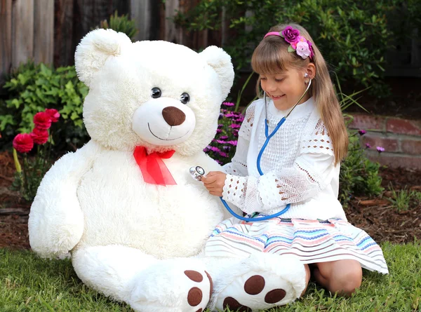 Smiling girl plays the doctor with huge toy white bear