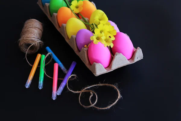 Цветные пасхальные яйца с яркими маркерами, веревкой и весенними желтыми цветами — стоковое фото