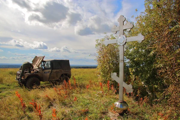 a man fixing a car on the background of a cross in a field