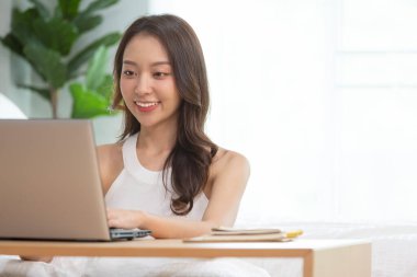 Evde yatağın üzerinde dizüstü bilgisayarda çalışan Asyalı bir kadın..