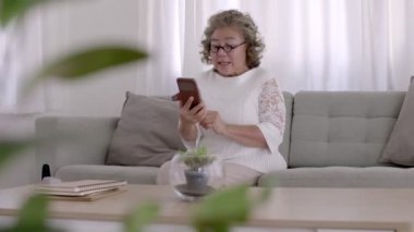 Yaşlı Asyalı kadın video konferansı evde akıllı telefonuyla çevrimiçi.