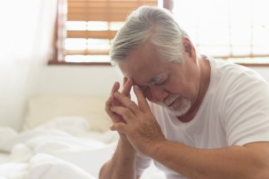 Baş ağrısı olan Asyalı yaşlı bir adam sabahları yatakta oturuyor.