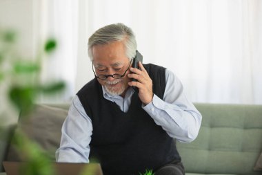 Asyalı yaşlı adam cep telefonu ve dizüstü bilgisayarda çalışıyor.