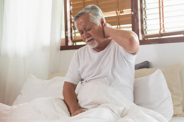 Asian Elderly man with a headache sitting on a bed in morning