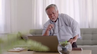Evde, oturma odasında dizüstü bilgisayarda çalışan Asyalı yaşlı bir adam..
