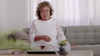 Asyalı yaşlı kadın oturma odasındaki kanepede kalp rahatsızlığı nedeniyle göğüs ağrısı çekiyor..