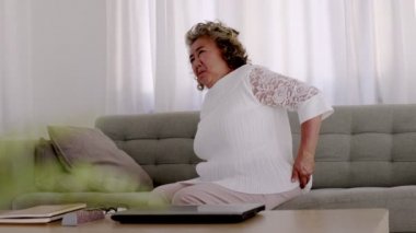Asyalı yaşlı kadının sırt ağrısı var. Oturma odasındaki kanepede..