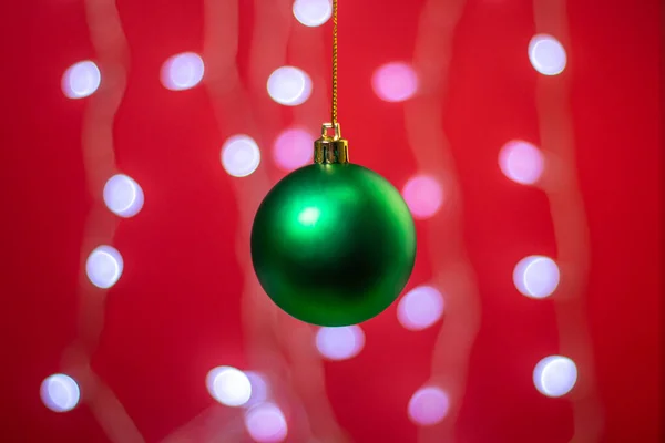 Green Christmas ball on a background of a glowing garland.  Christmas decorations on a red background. Holiday decorations. Christmas concept.