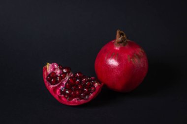 Siyah arka planda nar. Kesik Nar, bütünün yanında. Kırmızı meyve