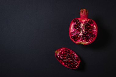 Siyah arka planda nar. Narı kes. Kırmızı meyve. Yukarıdan bir fotoğraf. Yazıt ya da logo için bir yer var.