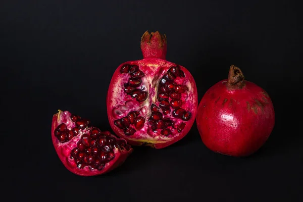 Pomegranate on a black background. The cut Pomegranate next to the whole. Red fruit