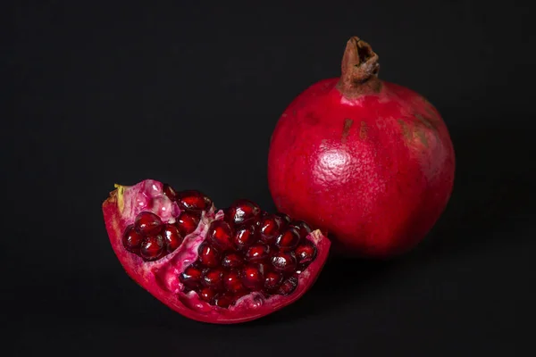 Siyah arka planda nar. Kesik Nar, bütünün yanında. Kırmızı meyve