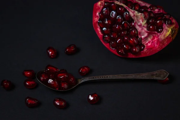 Pomegranate on a black background. Cut Pomegranate. Red fruit. Pomegranate full spoon