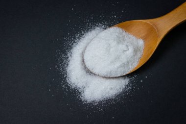 Tahta kaşık ve tuz. Yakınlarda biraz tuz dökülmüş. Aşırı tuz alımı. Kaba tuz.