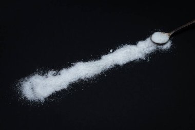 Siyah arka planda tuz. Tuz sırası, yanında bir kaşık var. Aşırı tuz alımı. Kaba tuz.
